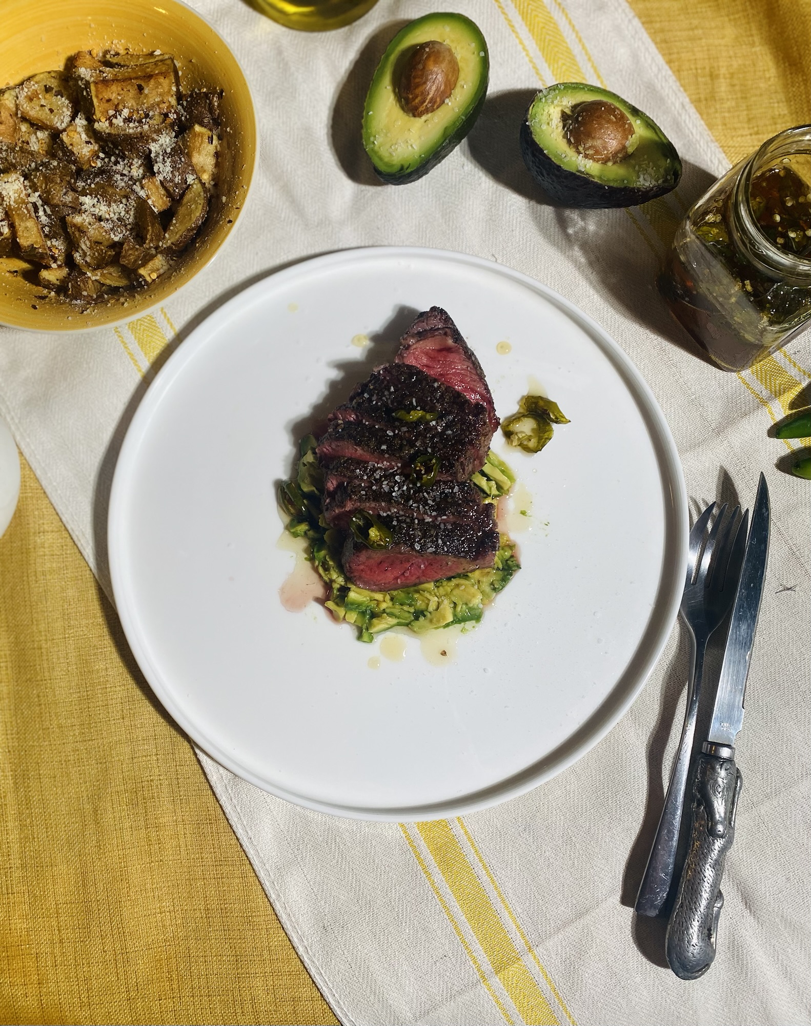 overhead shot of the new york strip steak plated over mashed avocado and drizzeled in serrano honey